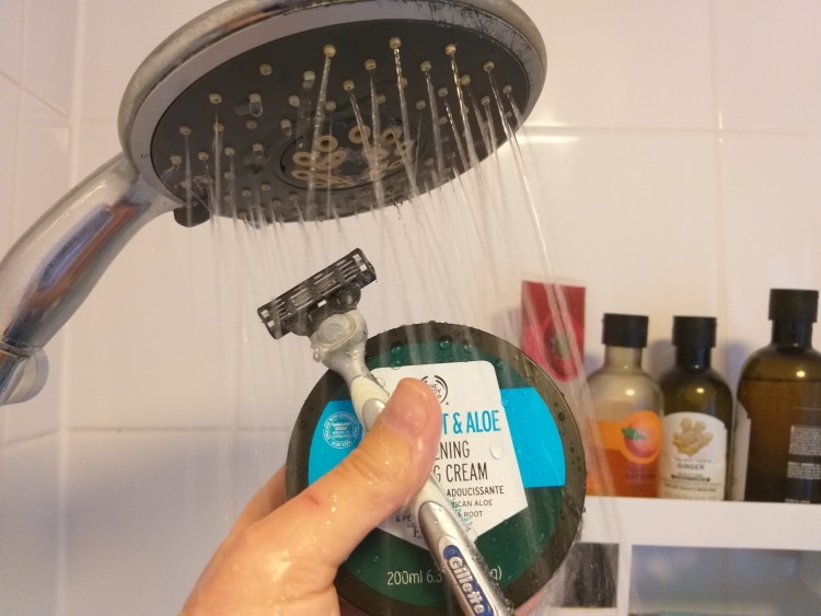 Gillette razor and shaving cream in hand under shower head ready to shave