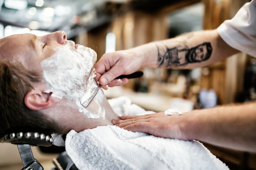 man being shaver at the barbers with a straight razor