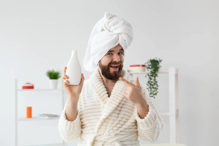 bearded man wearing bathrobe with hair conditioner in his hand