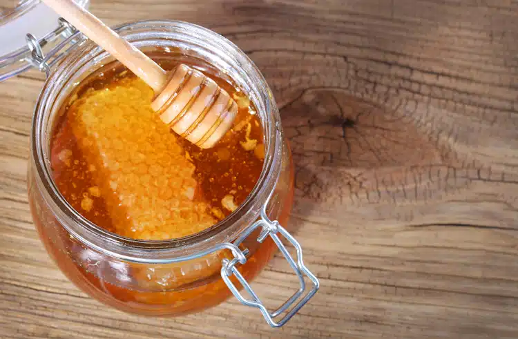 a jar of honey and honeycomb on wooden table