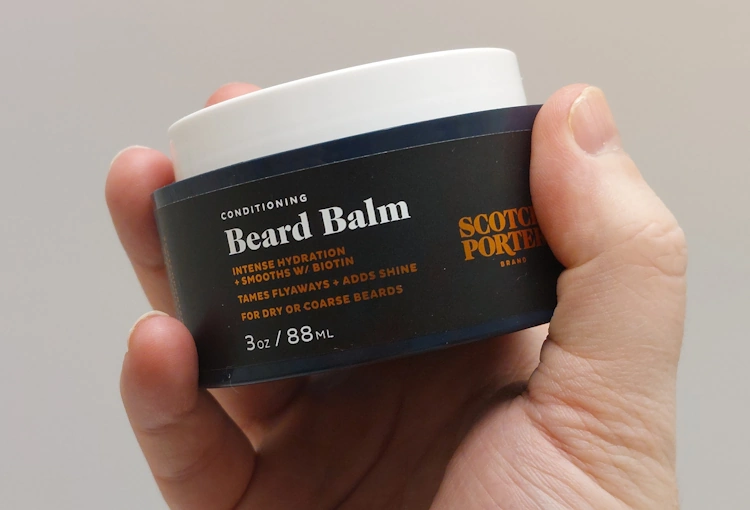 holding a tub of Scotch Porter Conditioning Beard Balm in the hand