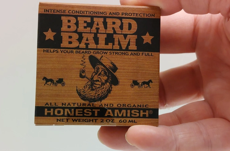 holding a box with Honest Amish Beard Balm inside