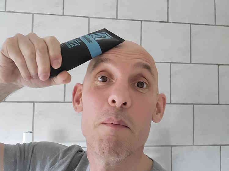Reviewer holding a tube of Headblade HeadLube matte lotion next to his head