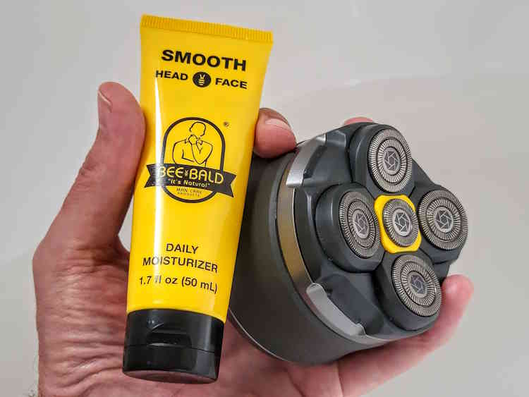 holding a tube of Bee Bald Smooth Daily Moisturizer and electric head shaver