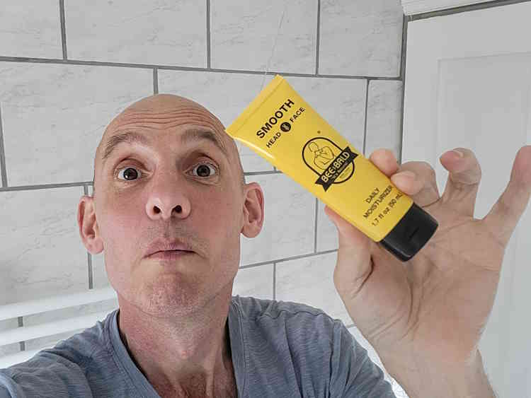 reviewer Jason holding a tube of Bee Bald Smooth Daily Moisturizer with a funny face