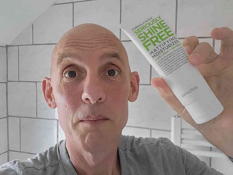 Jason the reviewer holding a tube of Formula 10.0.6 Seriously Shine Free Mattifying Moisturizer in the bathroom