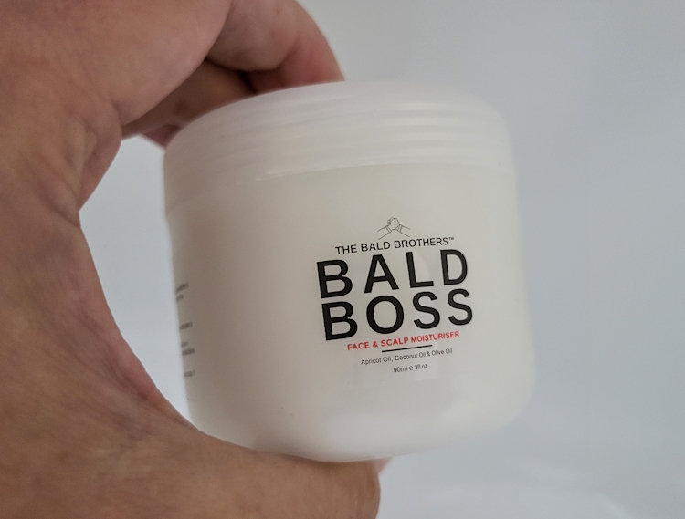 holding a tub of Bald Boss Face & Scalp Moisturiser