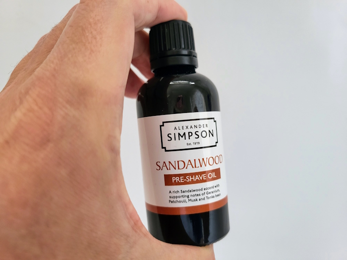 holding Simpson Sandalwood Pre-Shave Oil bottle between a finger and thumb