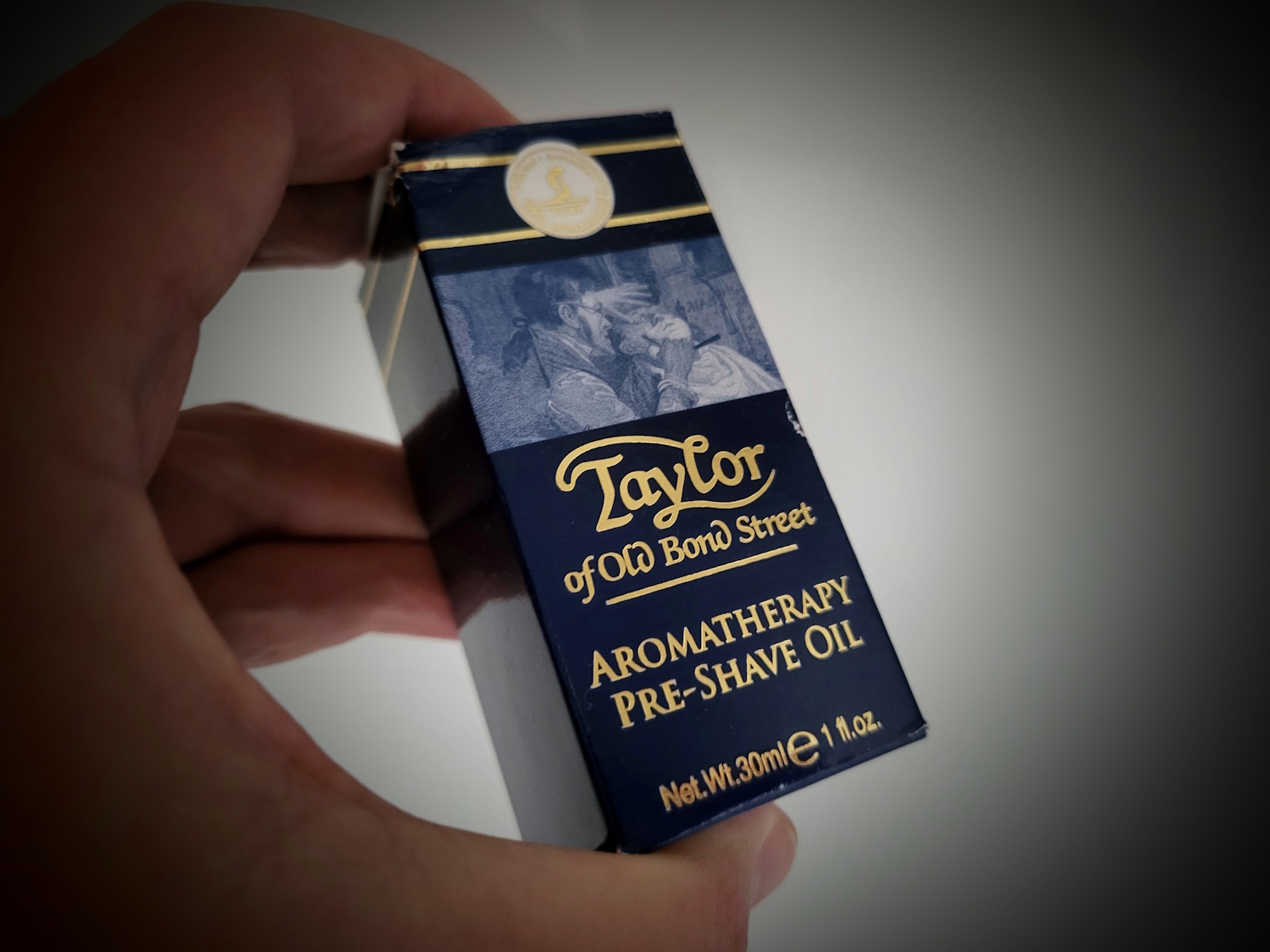 holding a bottle of Taylor of Old Bond Street Aromatherapy Pre-Shave Oil inside its box